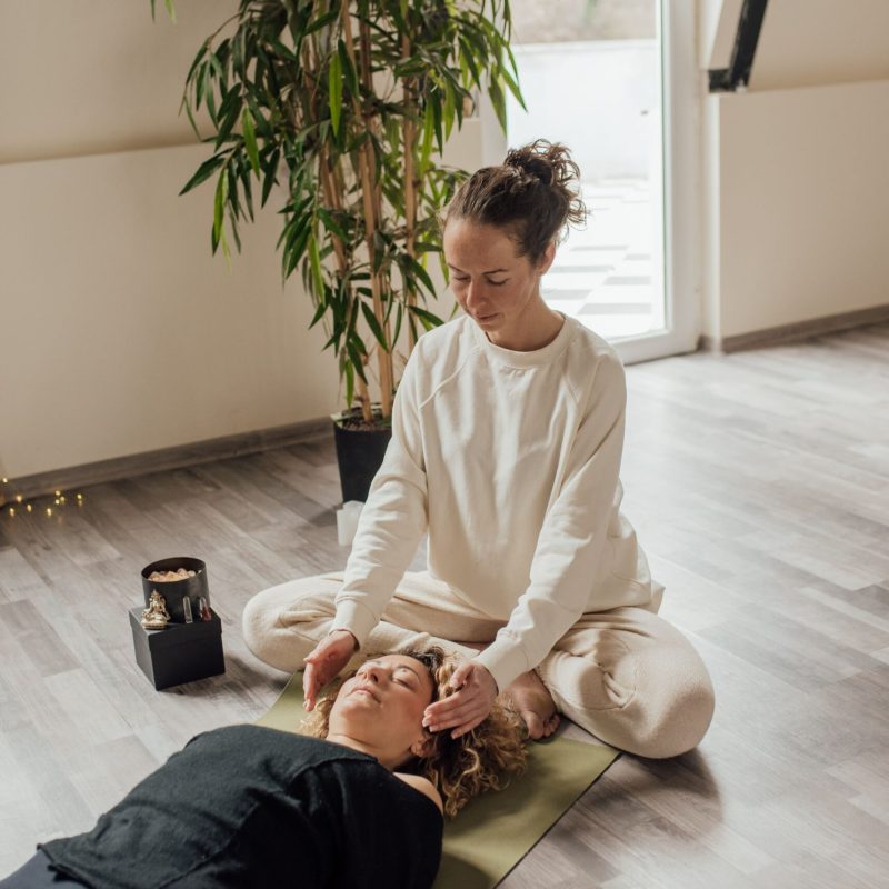 A calming Reiki session indoors with a therapist and patient on a yoga mat, focusing on healing energy.