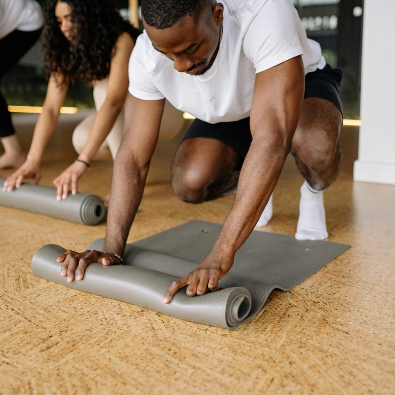 Diverse group of adults rolling yoga mats in a studio, preparing for exercise.
